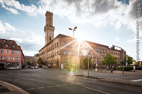 Ein repräsentatives Gebäude mit einem Turm, hinter dem gerade die Sonne aufblitzt